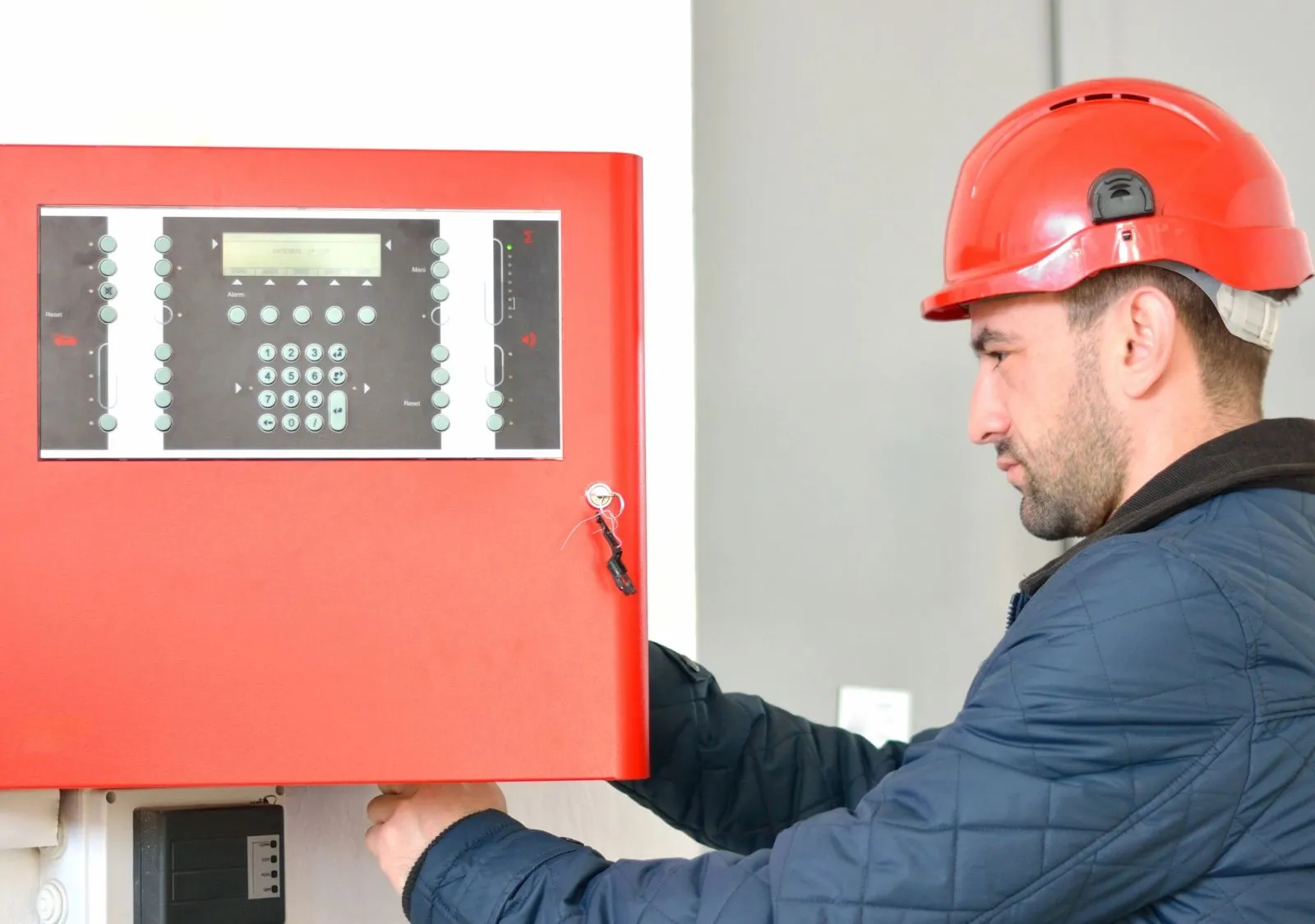 Technician in a hard hat working at a red fire alarm control panel