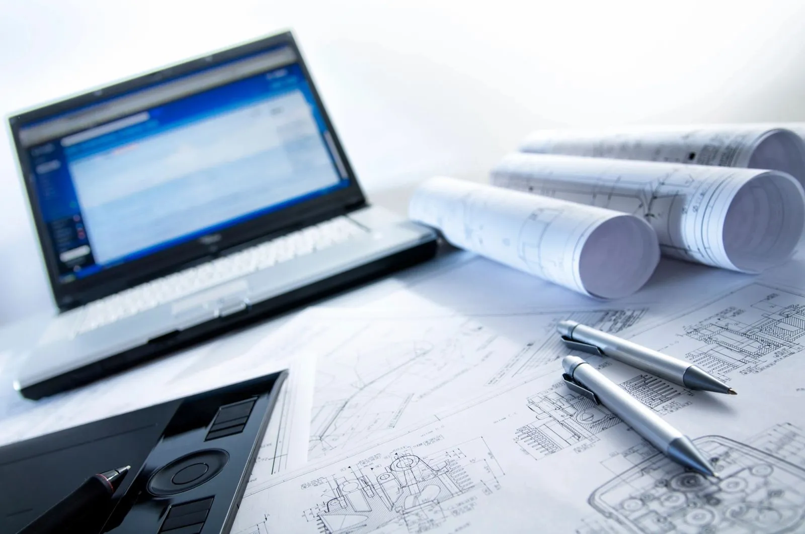 Rolled construction drawings and a laptop on a desk during a document review
