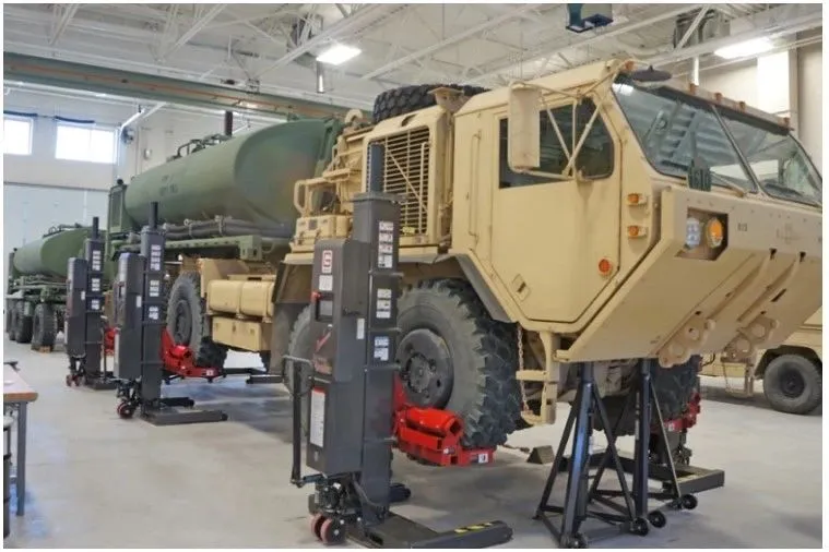 Military tactical vehicles raised on lifts inside a maintenance bay
